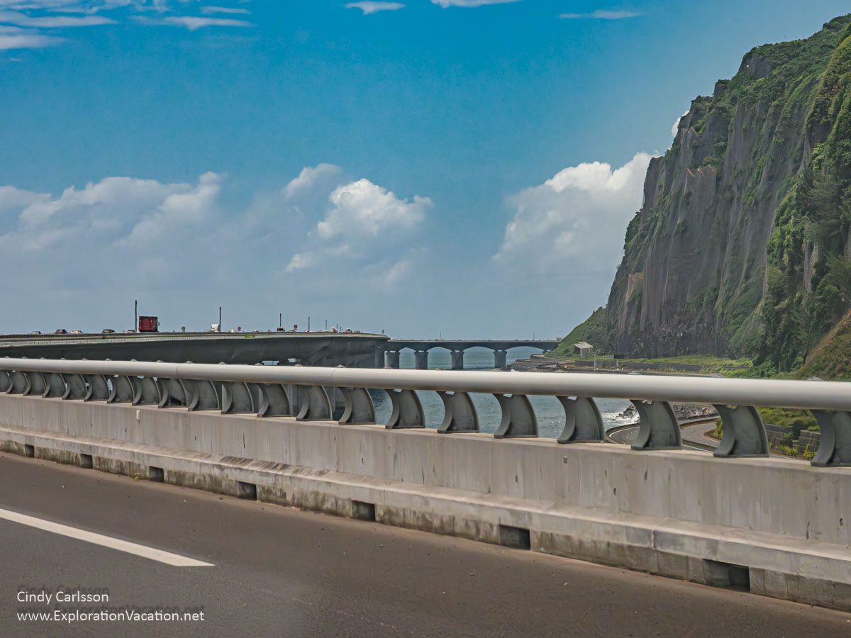 A road built on viaducts over the sea with cliffs along the shore as seen from the road itself.