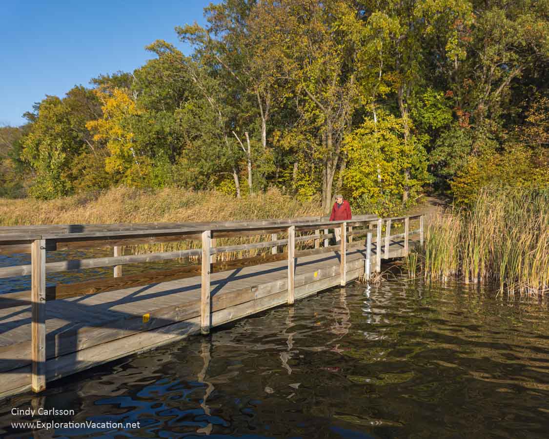 A dock with a colorful fall forest along the shore.