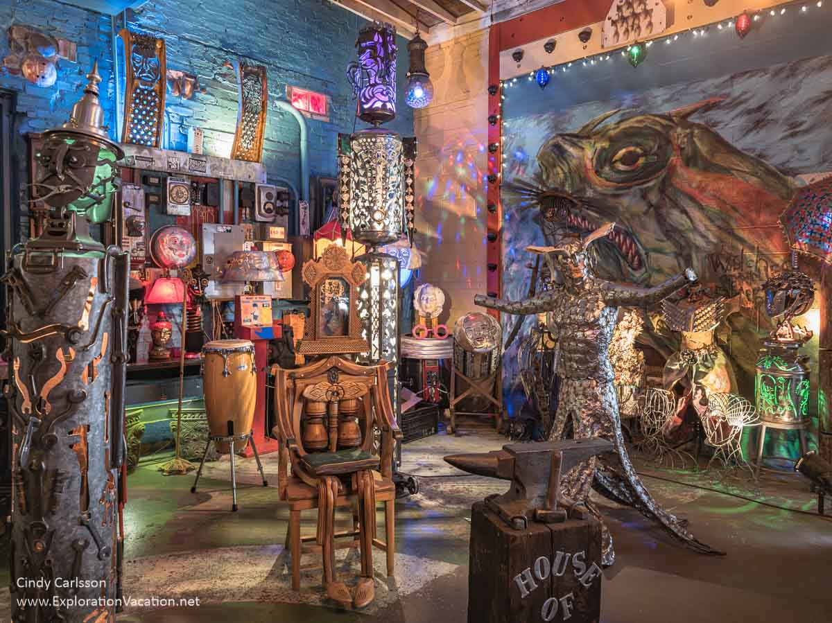 A gallery in the House of Balls with sculptural and mechanical beings, colorful lamps, a giant sea monster mural on the wall, and more.
