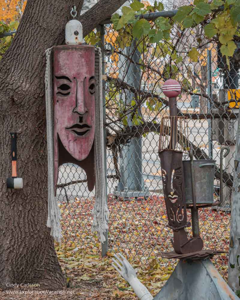A giant chime or bell with a woman's face and a metal sculpture of a woman in the fenced yard along the building.